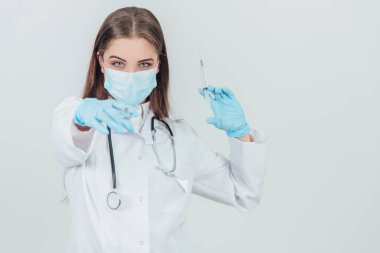 Tıbbi maskeli kötü kadın doktor elinde şırıngalarla birini kameraya doğrultuyor..