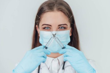 Tıbbi maskeli güzel kadın doktor kameranın önünde iki şırınga kesiyor..