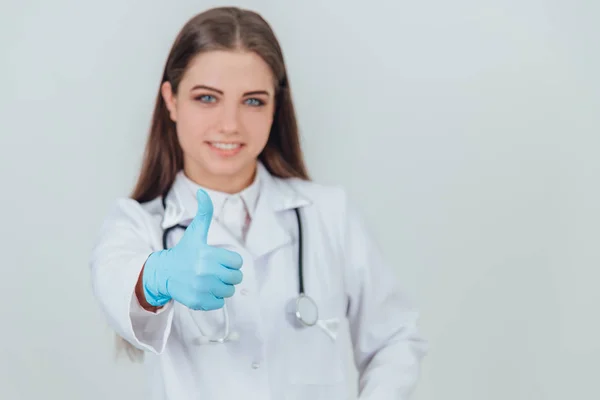 受到启发的年轻女性从业者站在那里，穿着医疗制服，对着相机微笑，放弃大拇指. — 图库照片