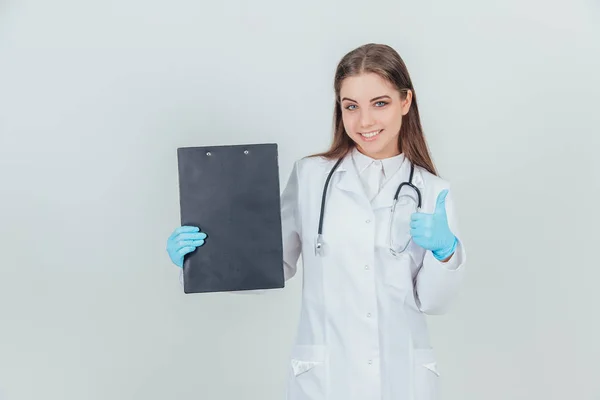 Inspirado jovem estagiária de pé em uniforme médico, segurando prancheta, dando o polegar para cima, mostrando sua aprovação . — Fotografia de Stock