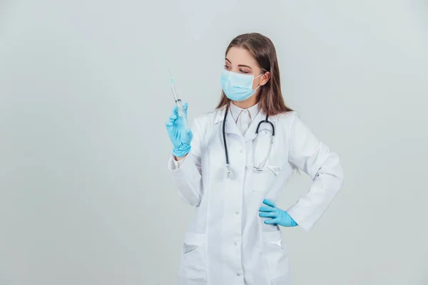 Vážná žena lékař v lékařské masce drží stříkačku, ruka akimbo. — Stock fotografie