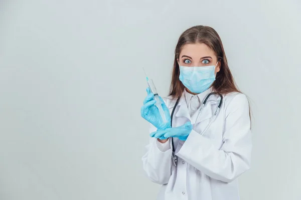 Docela vážná doktorka v lékařské masce drží stříkačku, dívá se široce otevřenýma očima. — Stock fotografie