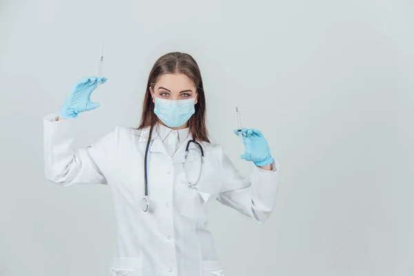 Впевнена красива серйозна жінка-лікар в медичній масці, що піднімає два шприци . — стокове фото
