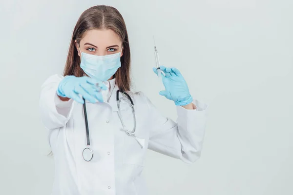 Zlá doktorka v lékařské masce, která drží stříkačky a míří jednou z nich na kameru. — Stock fotografie