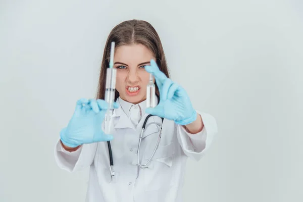 Strange female doctor holding her hands with syringes in front of camera, looking crazily. Blurred needles on the forefront. — ストック写真