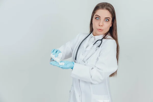 Hezká mladá internistka si nalévá pilulky z láhve do dlaně, oblečená v rukavicích na jedno použití. Široce otevřené oči. — Stock fotografie