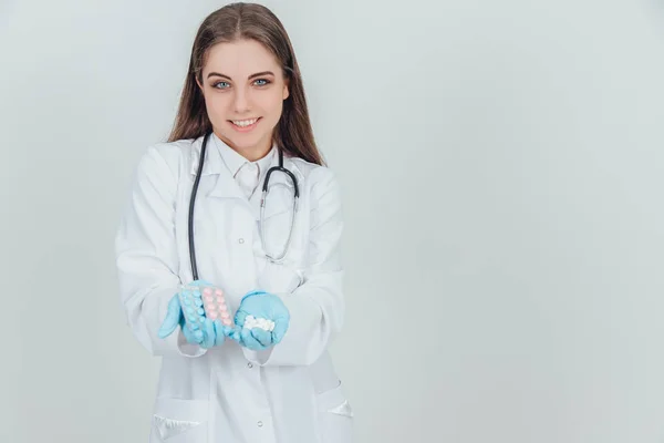 Adorável jovem enfermeira de pé com uma palma cheia de comprimidos brancos. Dois blisterpacks de comprimidos coloridos em outra palma . — Fotografia de Stock