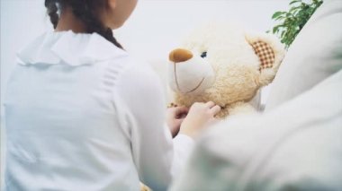 Güzel kız oyuncak ayısının papyonunu düzeltiyor ve peluş arkadaşını öpüyor. Ayıya odaklan..