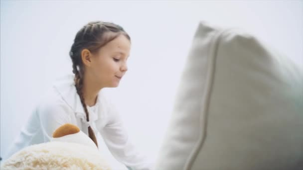 Gadis kecil dengan plaits menempatkan teddy putih di sofa, menutupinya dengan selimut, akan pergi . — Stok Video