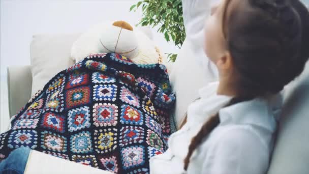 Linda niña sentada con las piernas acurrucadas, leyendo cuentos de hadas para su peluche, moviendo sus manos emocionalmente, mostrando la trama del libro . — Vídeos de Stock