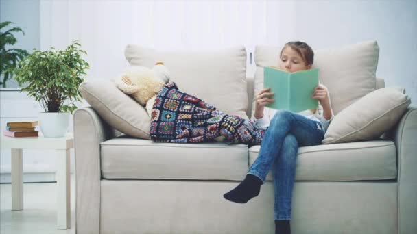 Mooi klein meisje leest sprookjes voor haar teddybeer, kust hem, zegt welterusten. — Stockvideo