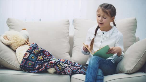 Hübsches kleines Mädchen liest Märchen für ihren Teddybär, streichelt ihn, schließt das Buch, sagt Gute Nacht, schläft auf dem weichen Bären ein. — Stockvideo