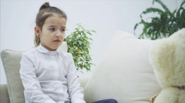Kanepede oturan tatlı küçük kız, ayısıyla konuşuyor. Bu onu anlamaz. Hayal kırıklığına uğramış görünüyor..