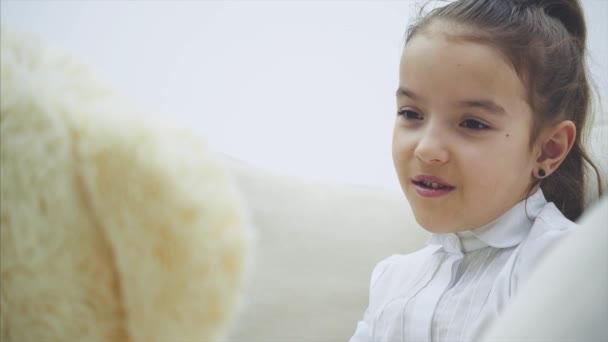 Adorable niñita sentada en el sofá, hablando con su peluche . — Vídeos de Stock