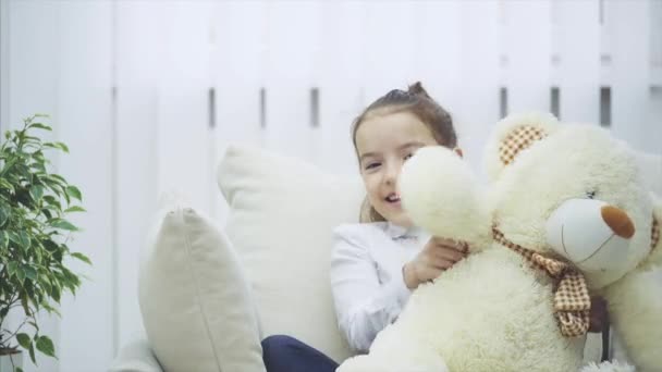 Kind en teddy op de bank. prachtig meisje is spelen met haar zachte vriend. — Stockvideo
