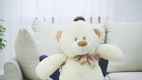 Grappig klein meisje verschuilt zich achter een grote witte teddybeer, zwaait met zijn poten, dan apperend en knuffelend. — Stockvideo
