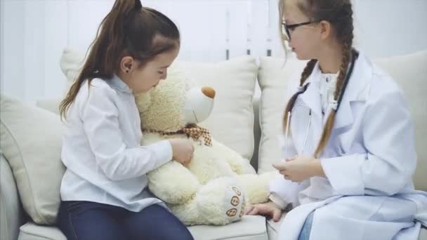 Little girl brought her teddy-bear to the doctor. Doctor is examining plush bear with stethoscope. — Stock Video