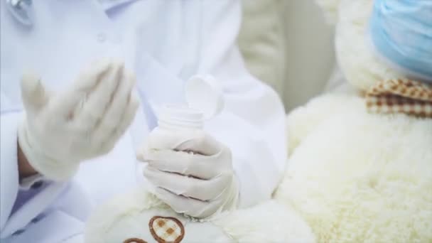 Обрезанные руки маленького доктора, выливающего таблетку из бутылки и дающего ее плюшевому мишке . — стоковое видео