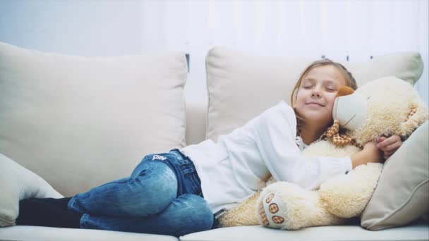 Χαριτωμένο κοριτσάκι ξαπλωμένο στον καναπέ, αγκαλιάζοντας το μεγάλο της αρκουδάκι.. — Αρχείο Βίντεο