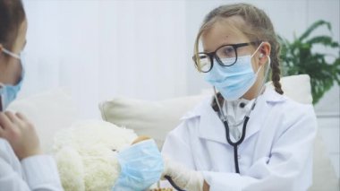 Oyuncak ayıyla oynayan iki tatlı çocuk. Pelüş ayıyı steteskopla inceleyen doktorlar..
