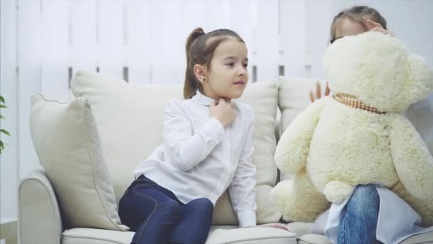 Zwei süße Kinder spielen mit Teddybär. Ein Mädchen ist Ärztin und untersucht Plüschbär. — Stockvideo
