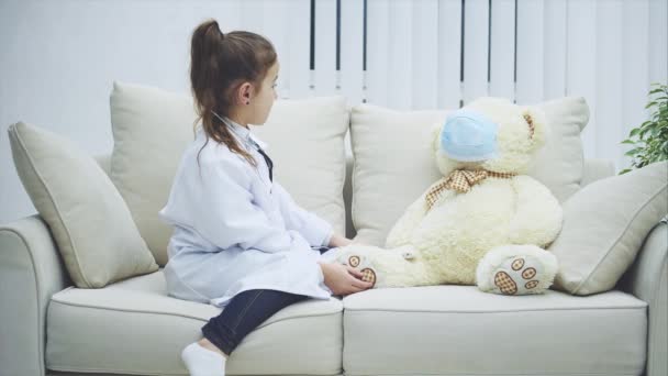 Holčička si hraje se svým medvídkem. Je to doktorka. Medvěd je pacient. Dívka zkoumá svého medvídka se stetoskopem. — Stock video