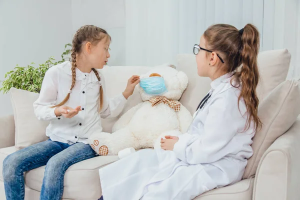 Little doctor prescribed pills for ill teddy bear and is explaining how to take med. Another girl is holding pills in her palm, listening to the doctor. — Stock Photo, Image