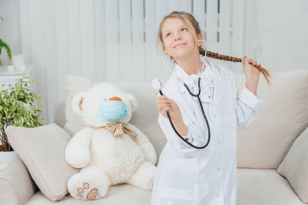 Pretty confident little girl wearing doctor coat, holding stethoscope, pulling her beautiful plait, standing, posing.