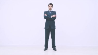 Ciddi yakışıklı iş adamı ayakta duruyor, ellerini kavuşturuyor, başparmağını kaldırıyor, kameraya güvenle bakıyor..
