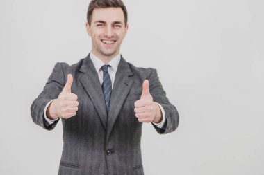 Yakışıklı iş adamı ayakta, baş parmağını kaldırıyor, gülümsüyor, memnuniyetini gösteriyor. Öndeki başparmaklara odaklan..