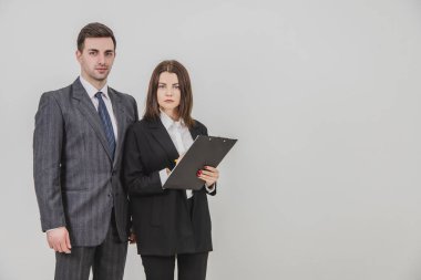 İş ortakları takım elbise giyiyor, yan yana duruyor, kameraya bakıyor, gülümsüyor. Kadın elinde bir dosya tutuyor..