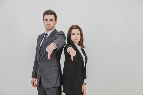 Business man and woman standing back to back, giving thumbs down, frowning.