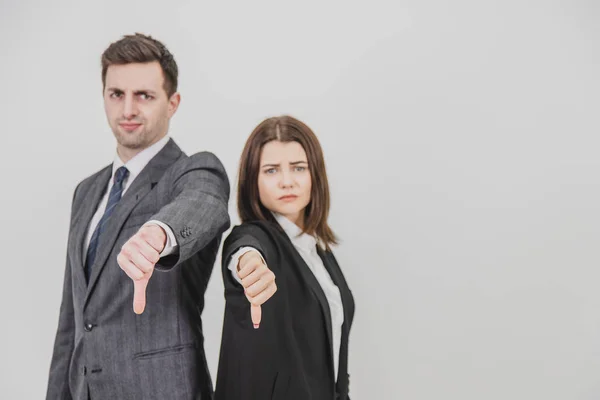 Hombre y mujer de negocios de pie espalda con espalda, dando pulgares hacia abajo, frunciendo el ceño. Concéntrese en el gesto en la vanguardia . — Foto de Stock