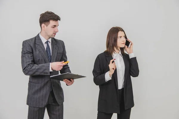 Przystojna, zajęta bizneswoman rozmawia przez telefon, wskazując palcem na sekretarkę. mężczyzna sekretarz stojąc z schowkiem, czekając dla bosss podpis. — Zdjęcie stockowe