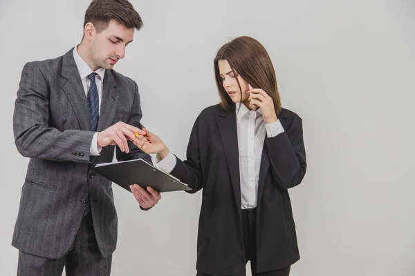 Beautiful busy businesswoman is talking on the phone, looking through document. Male secretary standing with clipboard, waiting for bosss signature. — Stock Photo, Image