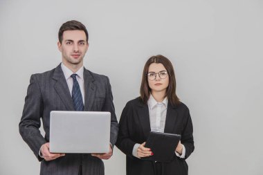 Genç iş çifti ayakta, dijital tablet ve dizüstü bilgisayarı birlikte kullanıyor..