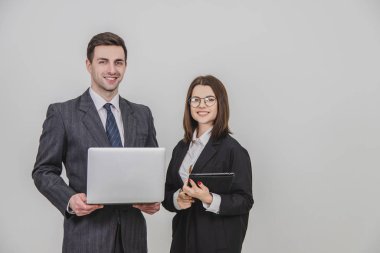 Genç iş çifti ayakta, dijital tablet ve dizüstünü birlikte kullanıyor, gülümsüyor..