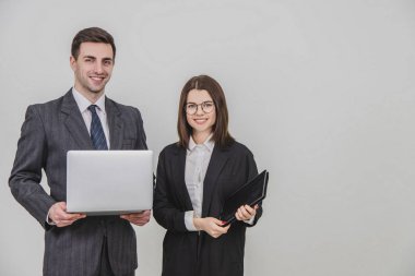 Genç iş çifti ayakta, dijital tablet ve dizüstünü birlikte kullanıyor, gülümsüyor..