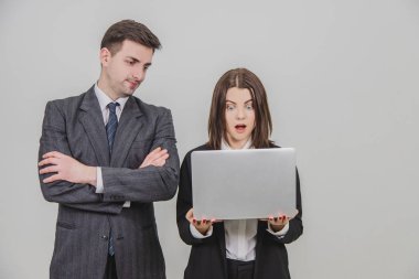 İş kadını dizüstü bilgisayar kullanıyor, heyecanlı bir yüz ifadesiyle bakıyor. Yanındaki adam elleri bağlı, canı sıkkın görünüyor..