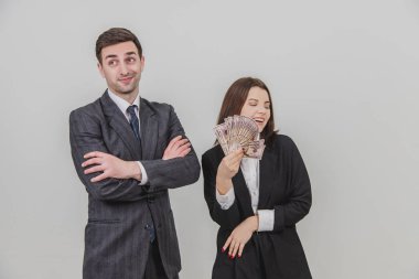 Güler yüzlü, kendine güvenen iş çifti. Adam elleri bağlı ayakta duruyor. Onun tarafındaki kadın, dolar banknotlarının hayranı tarafından rüzgâr yapıyor..
