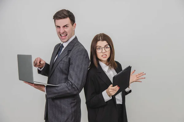 Busy successful work partners standing shoulder to shoulder, checking data. Man working with laptop, looking with irritated face expression, woman with tablet, setting her teeth. — Stock Photo, Image