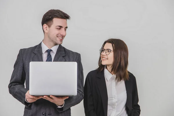 İş çifti. Adam dizüstü bilgisayar tutuyor, kadın yanında duruyor. Birbirlerine bakıp gülümsüyorlar.. — Stok fotoğraf