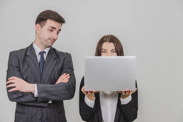 Bizneswoman używająca laptopa, patrząca na to z podniecającą miną. Mężczyzna po jej stronie, stojący ze złożonymi rękami, wyglądający na wkurzonego.. — Zdjęcie stockowe