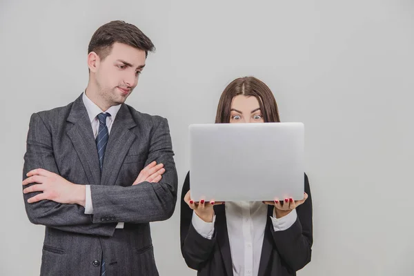 Bizneswoman używająca laptopa, patrząca na to z podniecającą miną. Mężczyzna po jej stronie, stojący ze złożonymi rękami, wyglądający na wkurzonego.. — Zdjęcie stockowe