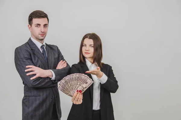 Blurred rich confident business couple. Man is standing with his hands folded. Woman on his side is extending a fan of dollar banknotes. — 图库照片