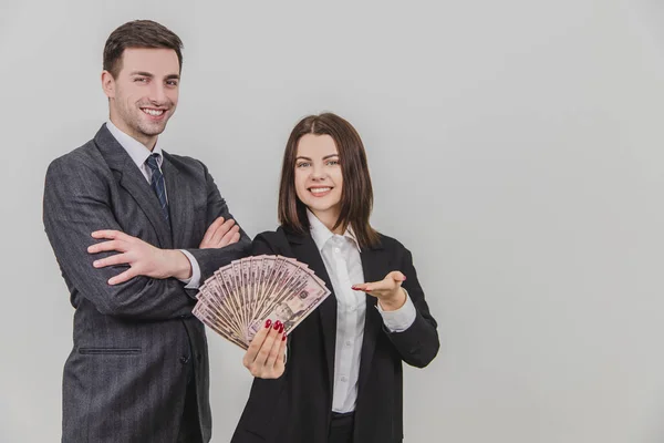 Sonriendo pareja de negocios ricos y confiados. El hombre está de pie con las manos cruzadas. Mujer de su lado está extendiendo un ventilador de billetes de dólar . — Foto de Stock