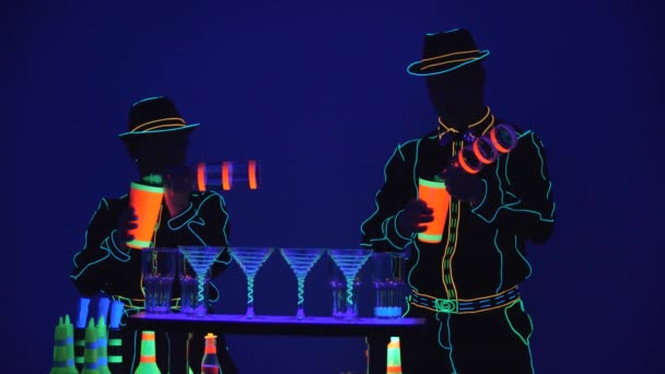 Espectáculo de Barmen. Desempenho. Barmaid e barman estão derramando álcool juntos, vestidos com uniforme de néon em fundo azul brilhante. Movimento lento. 4K . — Vídeo de Stock
