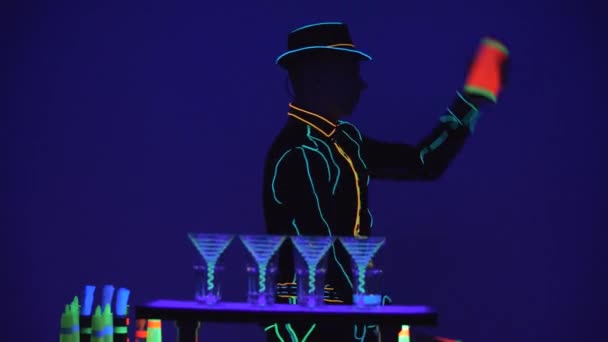 Шоу барменов. Выступление. Бармен жонглирует бутылками, а потом разливает алкоголь на ярко-голубом фоне. Медленное движение. 4K . — стоковое видео