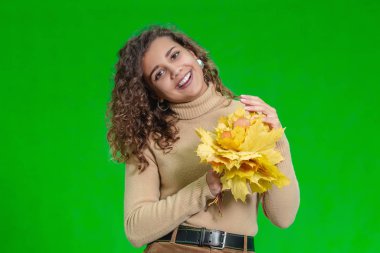 Yeşil arka plan ve neşeli Afro-Amerikalı kız poz veriyor, elleri parlak sonbahar yapraklarıyla dolu..