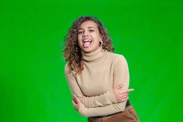 Porträtt av rolig kinky flicka sticker ut tungan framför kameran mot grön bakgrund. — Stockfoto